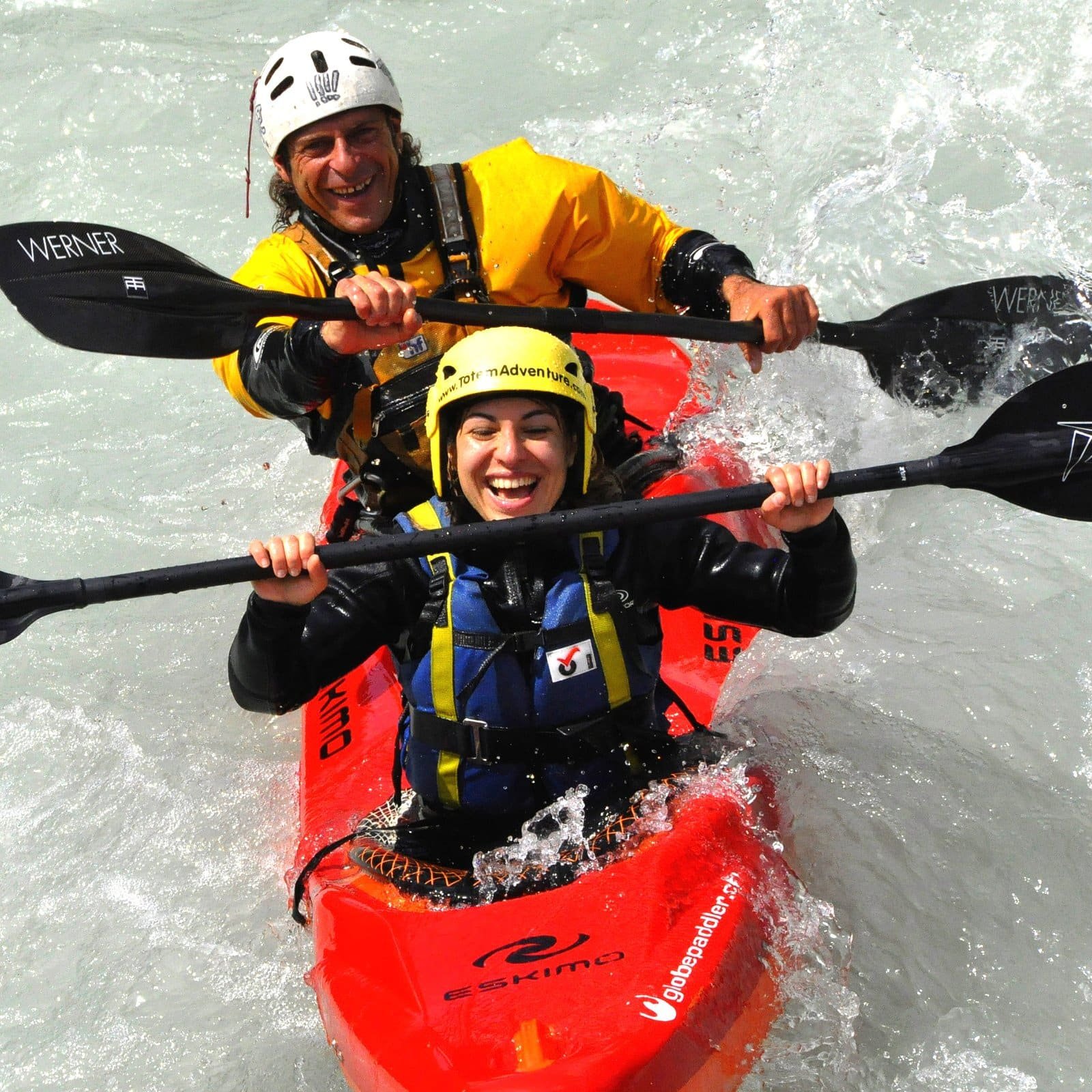 Totem Advenuture Two people wearing helmets and life jackets merrily navigate the rapids of a red tandem kayak, experiencing the exhilarating rapids of the renowned Aosta Valley waters. Rafting Kayaking Paragliding Canyoning Aosta Valley