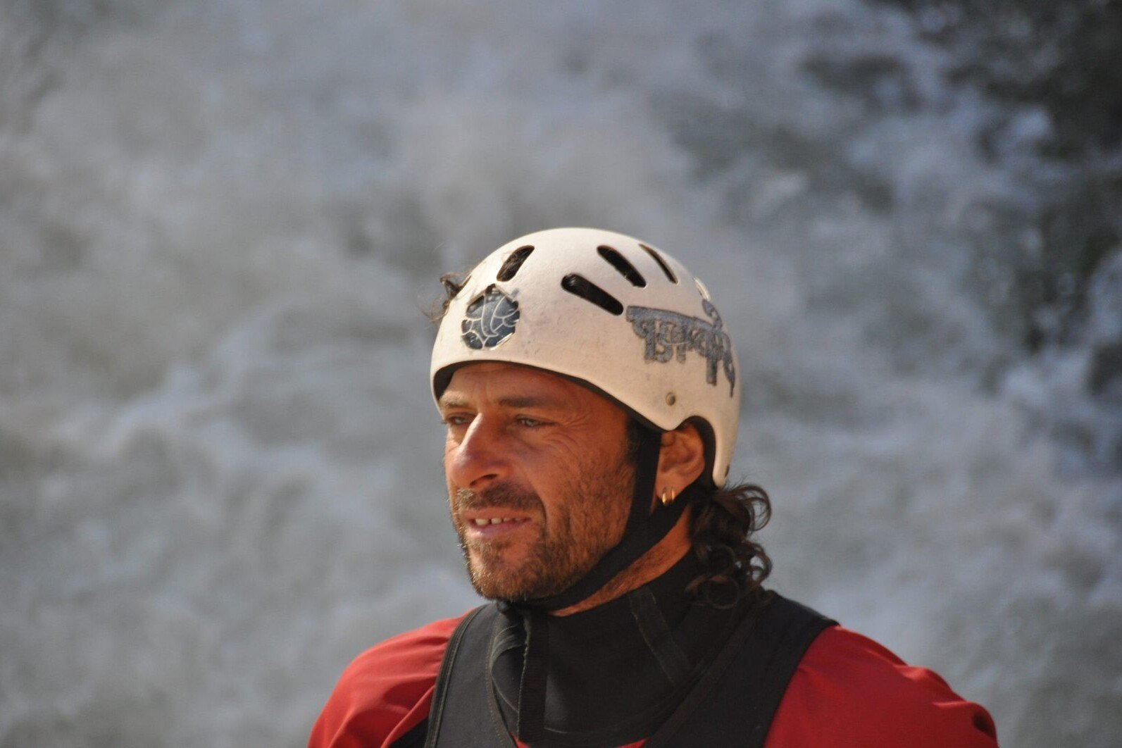 Totem Advenuture A man wearing a helmet and red jacket stands in front of a waterfall, enjoying the thrill of outdoor experiences in the Aosta Valley. Rafting Kayaking Paragliding Canyoning Aosta Valley