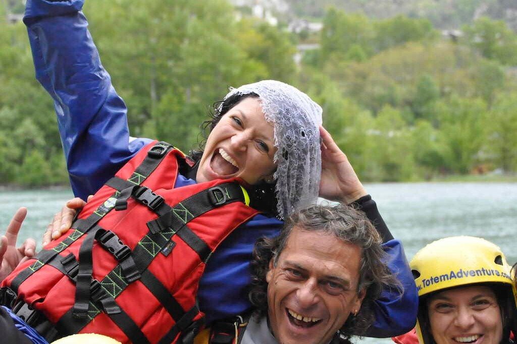 Totem Advenuture A group of people wearing life jackets and helmets laugh near a stretch of water, surrounded by trees. They are embracing the thrill of outdoor experiences in the Aosta Valley, perhaps after an exhilarating day of rafting. Rafting Kayaking Paragliding Canyoning Aosta Valley