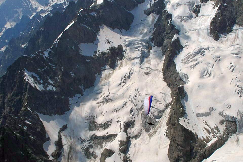 Totem Advenuture A paraglider flies gracefully over snow-capped mountains and rugged terrain, capturing the breathtaking beauty of the Aosta Valley near Pré-Saint-Didier. Rafting Kayaking Paragliding Canyoning Aosta Valley