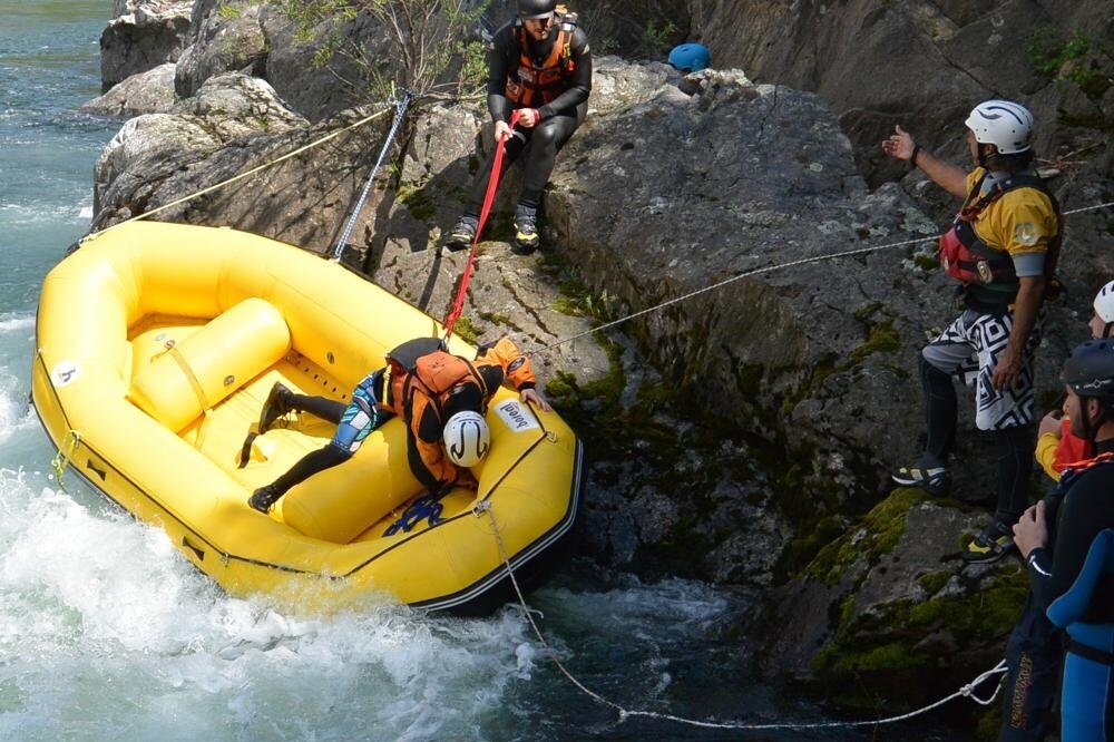 Totem Advenuture People wearing helmets are engaged in an adventurous rescue mission, pulling a yellow raft from the rocky riverbank using ropes, thus embodying the exciting outdoor experiences in Valle d'Aosta. Rafting Kayaking Paragliding Canyoning Aosta Valley