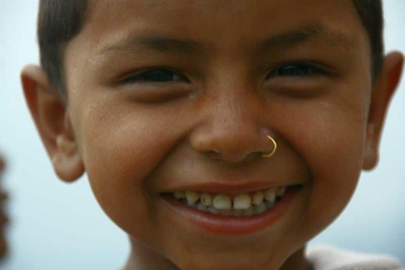 Totem Advenuture A child smiling broadly with a nose ring, conveying the emotion of an adventure, against a soft blue background reminiscent of rafting in Pré-Saint-Didier. Rafting Kayaking Paragliding Canyoning Aosta Valley