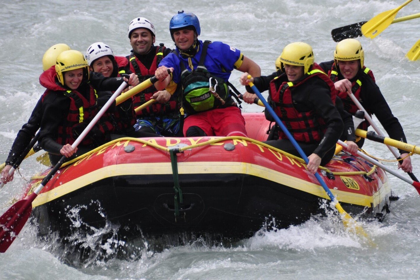Totem Advenuture A group of people, equipped with helmets and life jackets, enjoy an adventurous rafting experience on a rough river in the Aosta Valley. Rafting Kayaking Paragliding Canyoning Aosta Valley