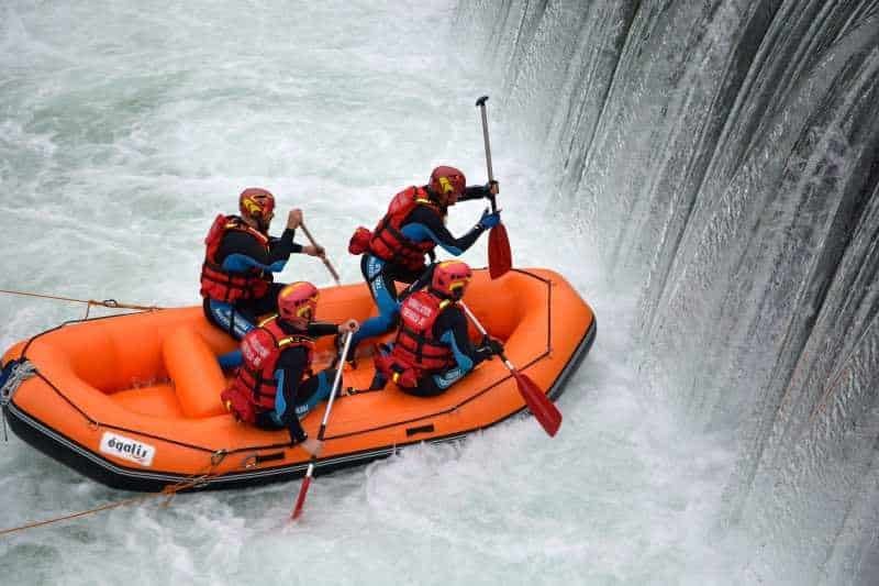 Totem Advenuture Four people aboard an orange inflatable boat skilfully tackle a waterfall while rafting in Valle d'Aosta, near Pré-Saint-Didier. Rafting Kayaking Paragliding Canyoning Aosta Valley