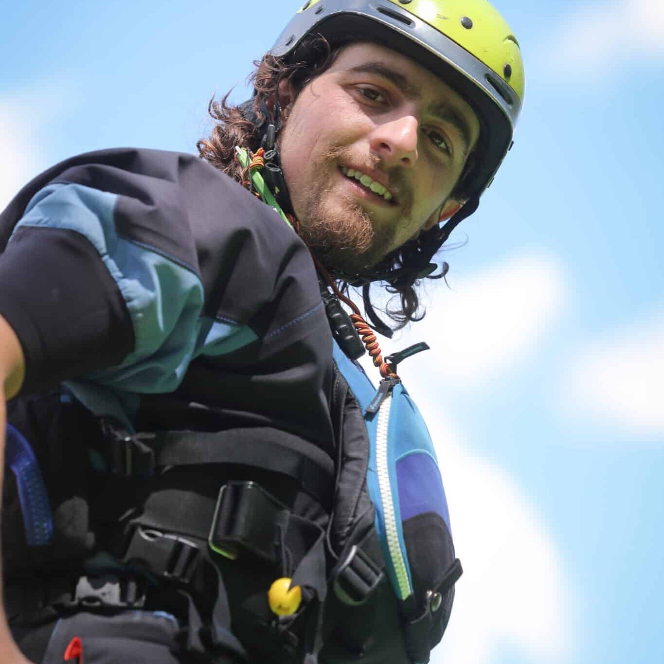 Totem Advenuture A man in helmet and outdoor gear smiles, ready for a Totem Team adventure, standing against a bright blue sky with clouds. Rafting Kayaking Paragliding Canyoning Aosta Valley