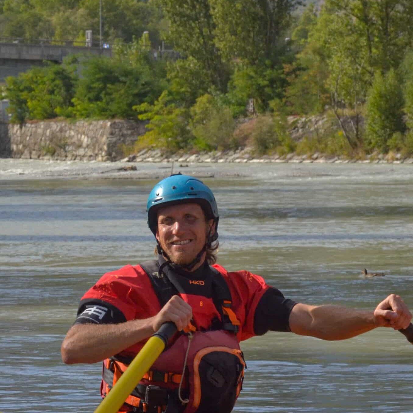 Totem Adventure Man with helmet and life jacket paddling on a red raft on a river, surrounded by trees and mountains, experiencing an exciting adventure by Team Totem. Rafting Kayaking Paragliding Canyoning Aosta Valley