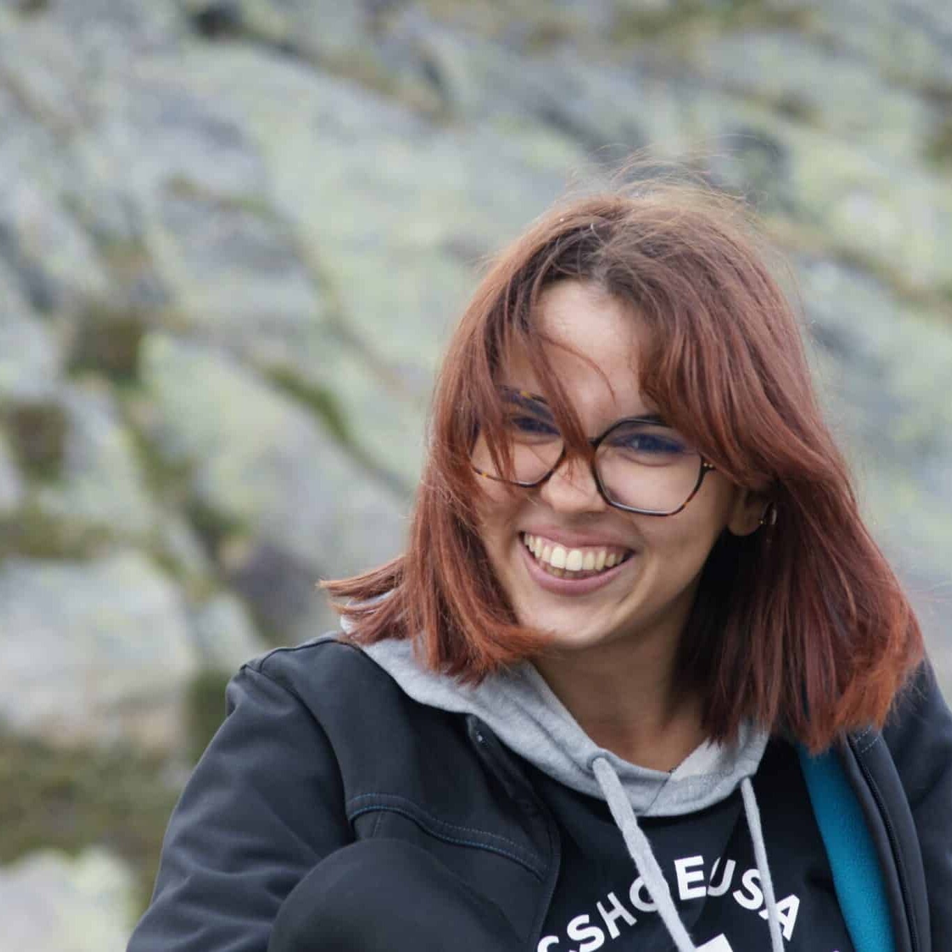 Totem Advenuture Una giovane donna con gli occhiali sorride all'aperto, con i capelli mossi dal vento, mentre si gode l'avventura di un totem di squadra su uno sfondo roccioso. Rafting Kayaking Parapendio Canyoning Valle d’Aosta