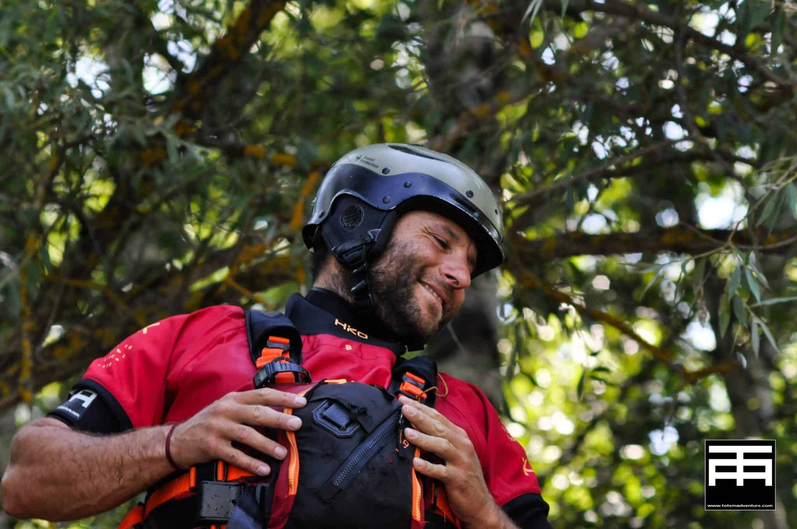 Totem Advenuture Un uomo in camicia rossa e casco sorride all'aperto, circondato da alberi frondosi, pronto per un'avventura del Team Totem. Rafting Kayaking Parapendio Canyoning Valle d’Aosta