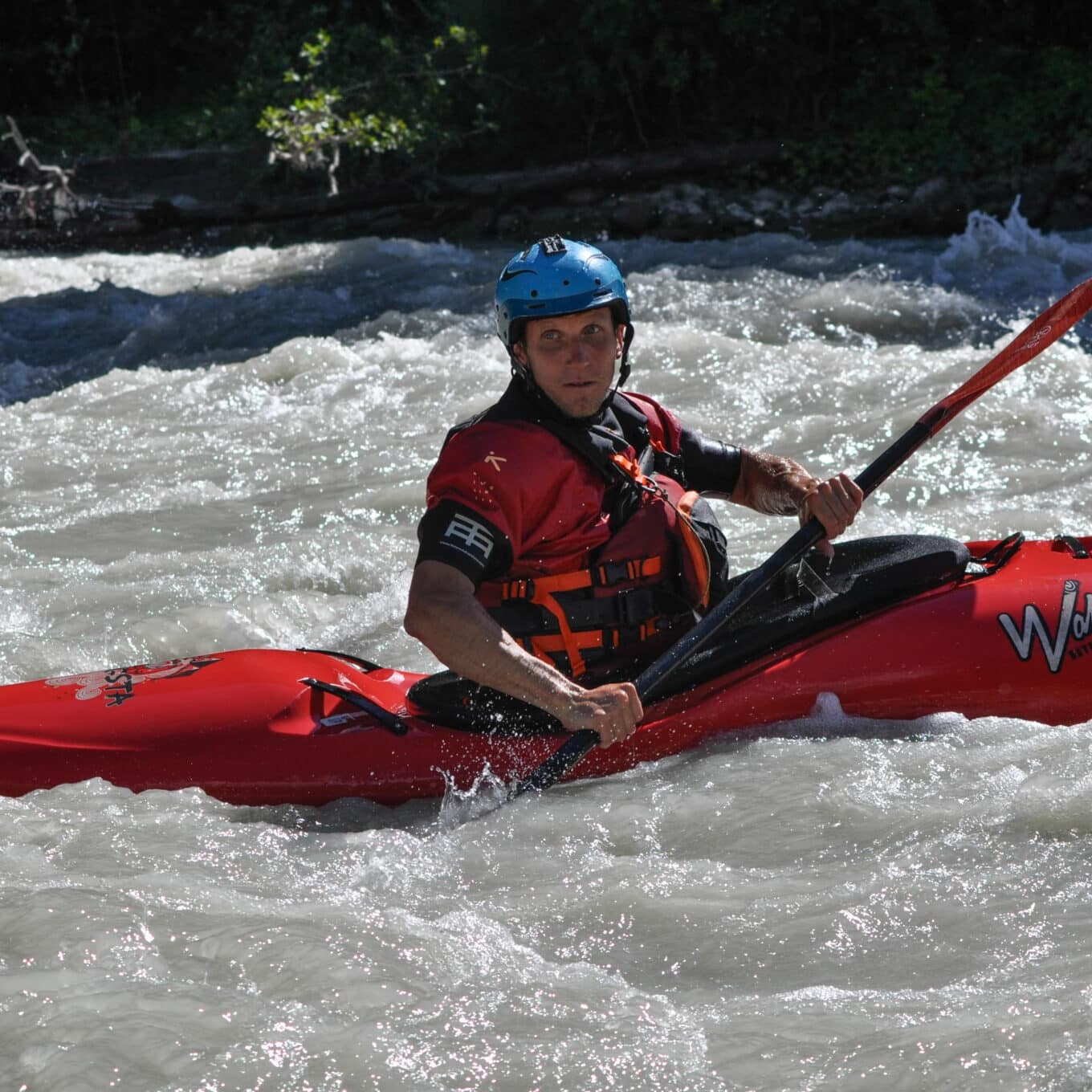 Totem Advenuture Una persona in un kayak rosso pagaia attraverso rapide d'acqua bianca in rapido movimento, indossando un casco e un giubbotto di salvataggio, abbracciando il brivido di un'avventura del Team Totem. Rafting Kayaking Parapendio Canyoning Valle d’Aosta