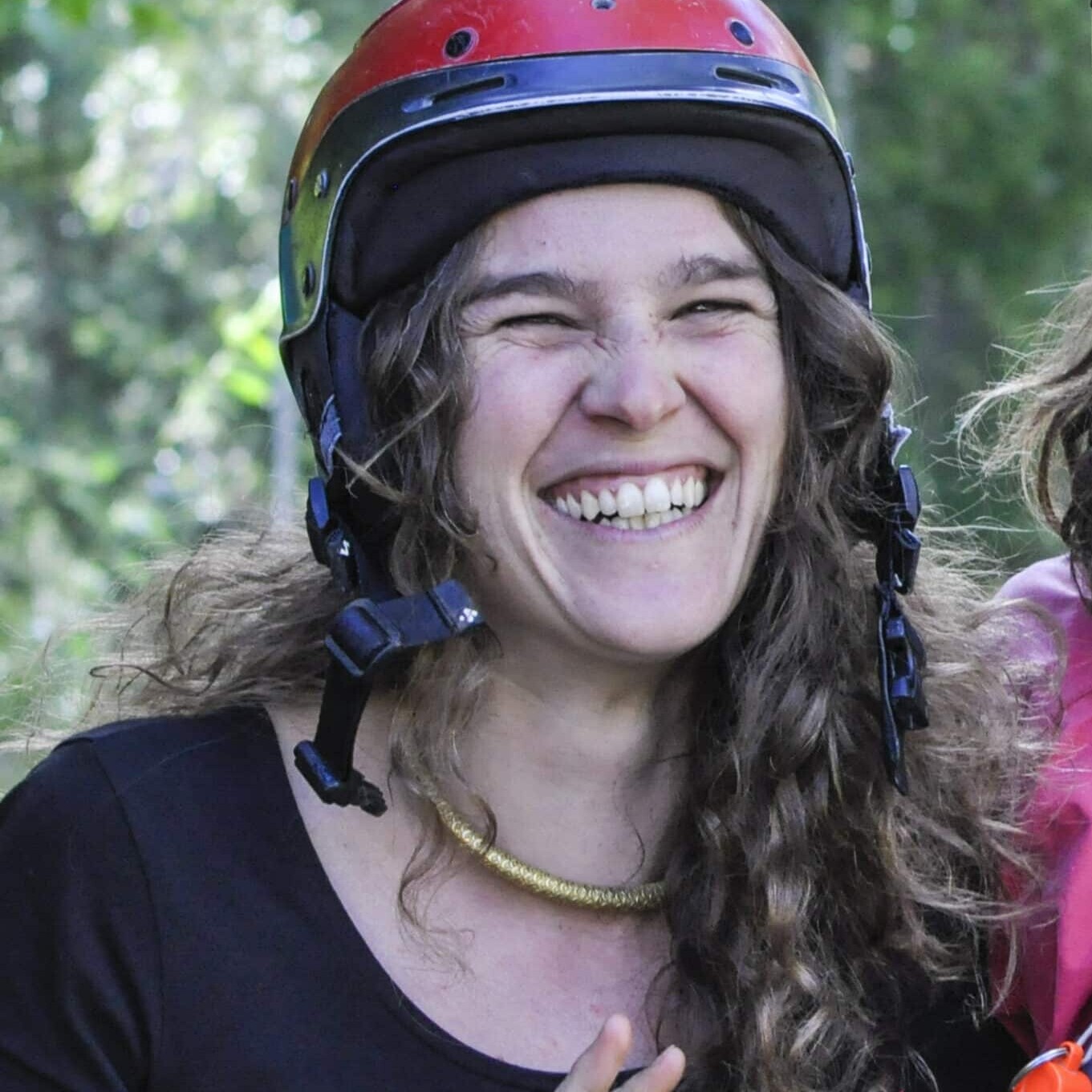Totem Advenuture Una donna sorridente con un casco rosso fa il segno della pace, in piedi all'aperto con alberi verdi sullo sfondo, pronta per la prossima avventura del Team Totem. Rafting Kayaking Parapendio Canyoning Valle d’Aosta