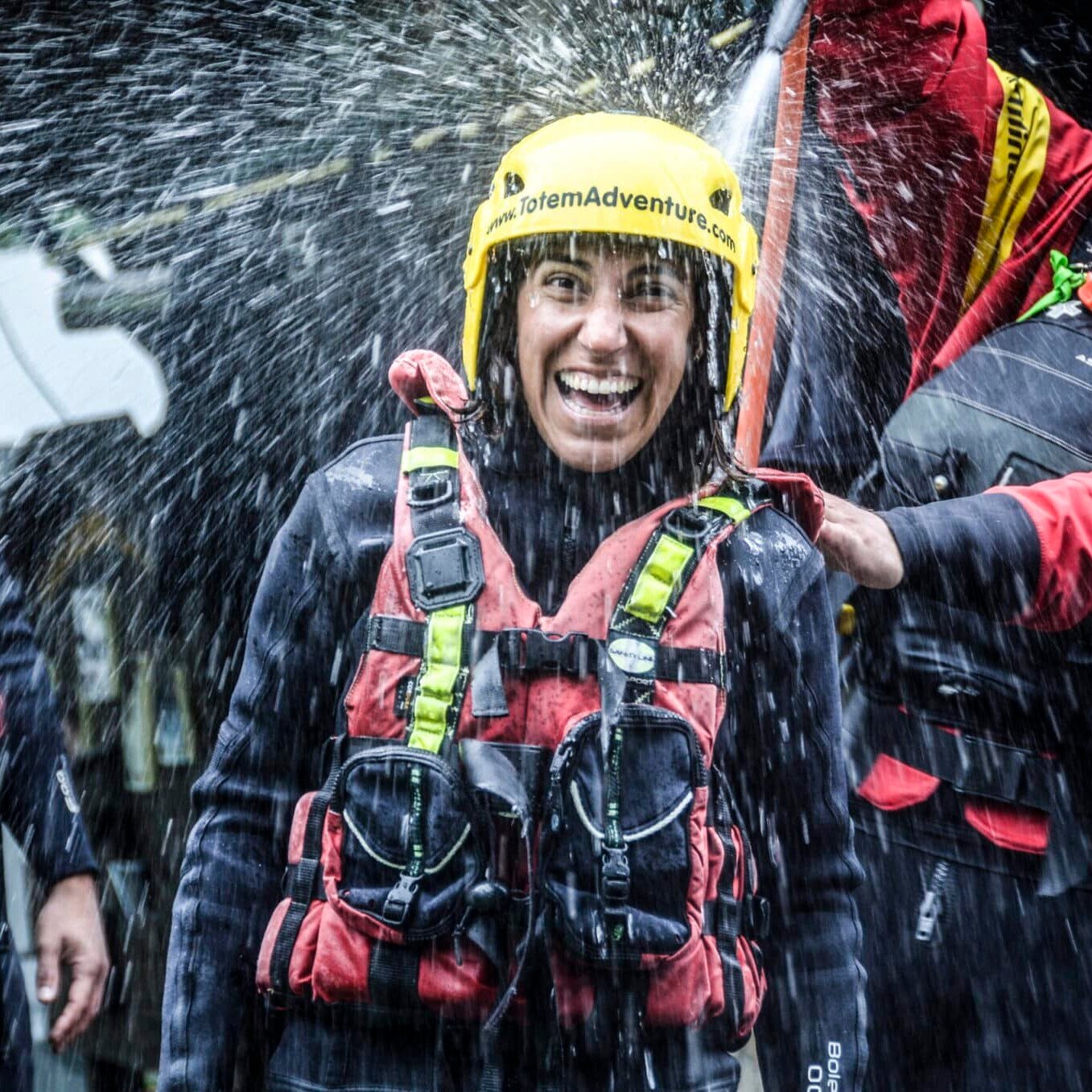 Totem Advenuture Una persona con casco e giubbotto salvagente ride mentre viene spruzzata d'acqua, circondata da altre persone con equipaggiamento simile durante un'emozionante avventura in kayak in Valle d'Aosta. Rafting Kayaking Parapendio Canyoning Valle d’Aosta