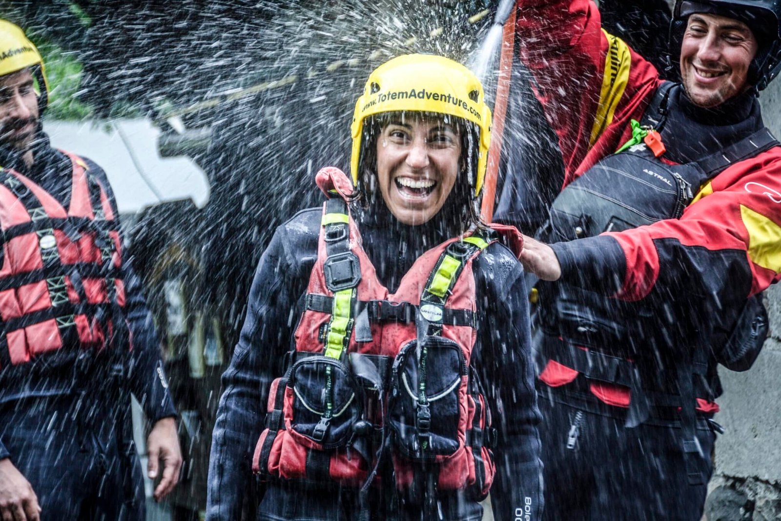 Totem Advenuture Una persona con casco e giubbotto salvagente ride mentre viene spruzzata d'acqua, circondata da altre persone con equipaggiamento simile durante un'emozionante avventura in kayak in Valle d'Aosta. Rafting Kayaking Parapendio Canyoning Valle d’Aosta
