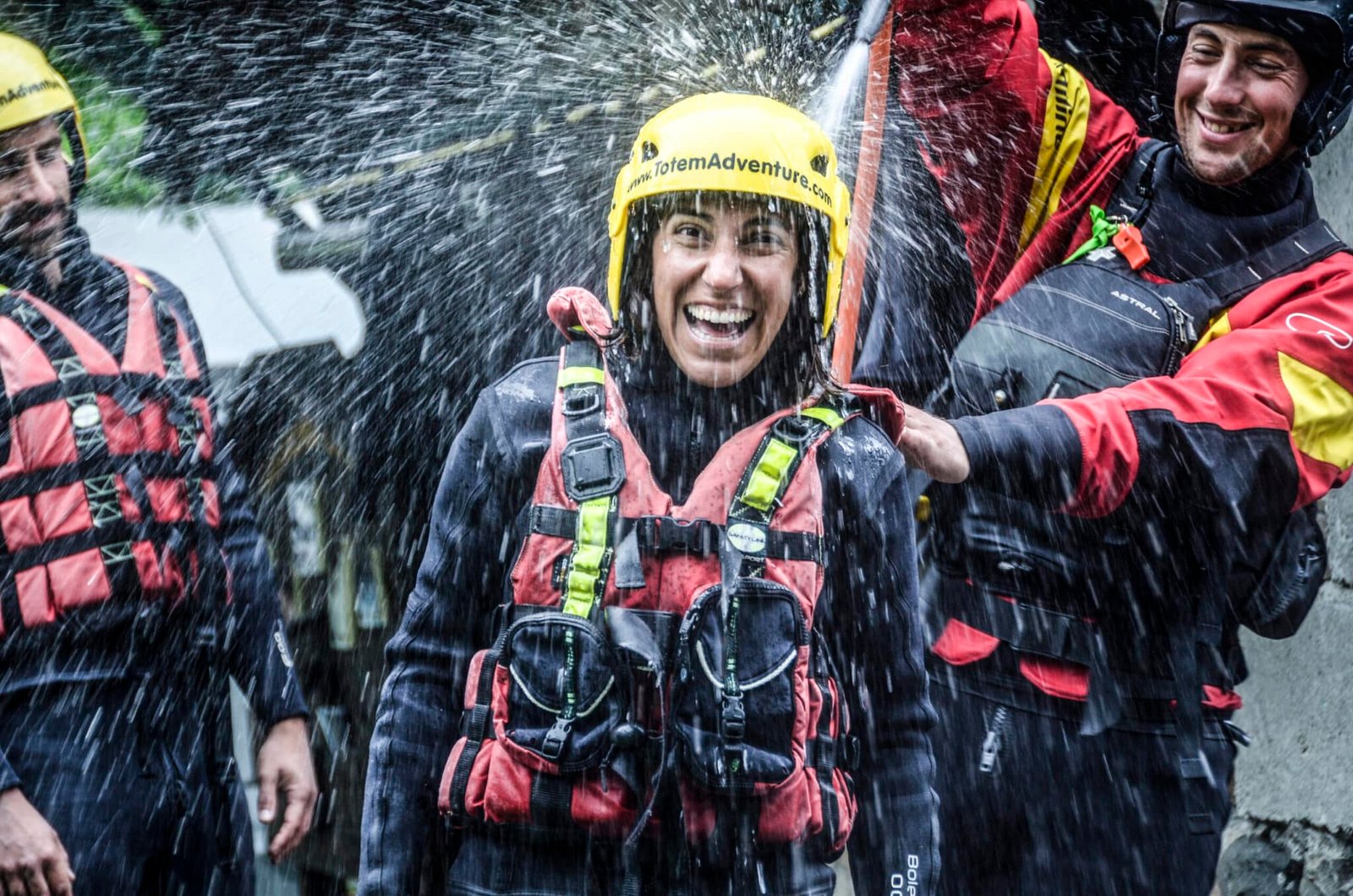 Totem Advenuture Una persona con casco e giubbotto salvagente ride mentre viene spruzzata d'acqua, circondata da altre persone con equipaggiamento simile durante un'emozionante avventura in kayak in Valle d'Aosta. Rafting Kayaking Parapendio Canyoning Valle d&rsquo;Aosta