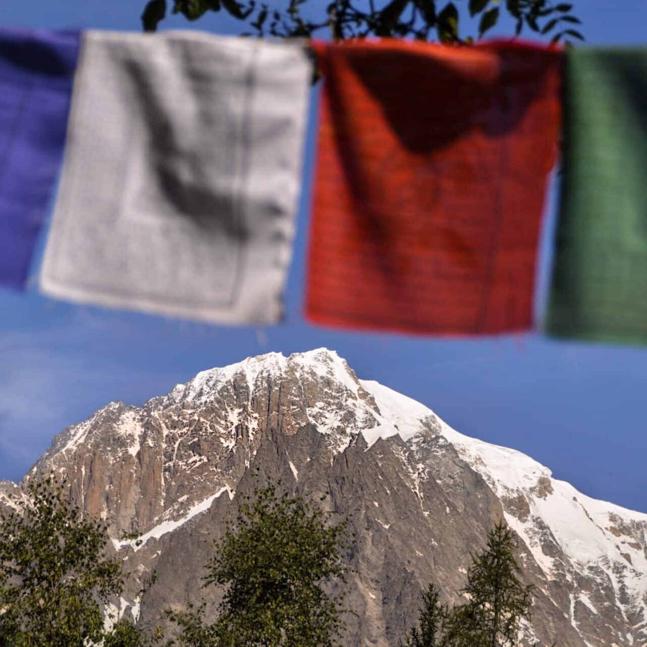 Totem Advenuture Bandiere di preghiera colorate sullo sfondo di montagne innevate sotto un cielo azzurro e limpido invitano all'avventura in Valle d'Aosta, dove vi attendono esperienze all'aria aperta come il kayak. Rafting Kayaking Parapendio Canyoning Valle d’Aosta