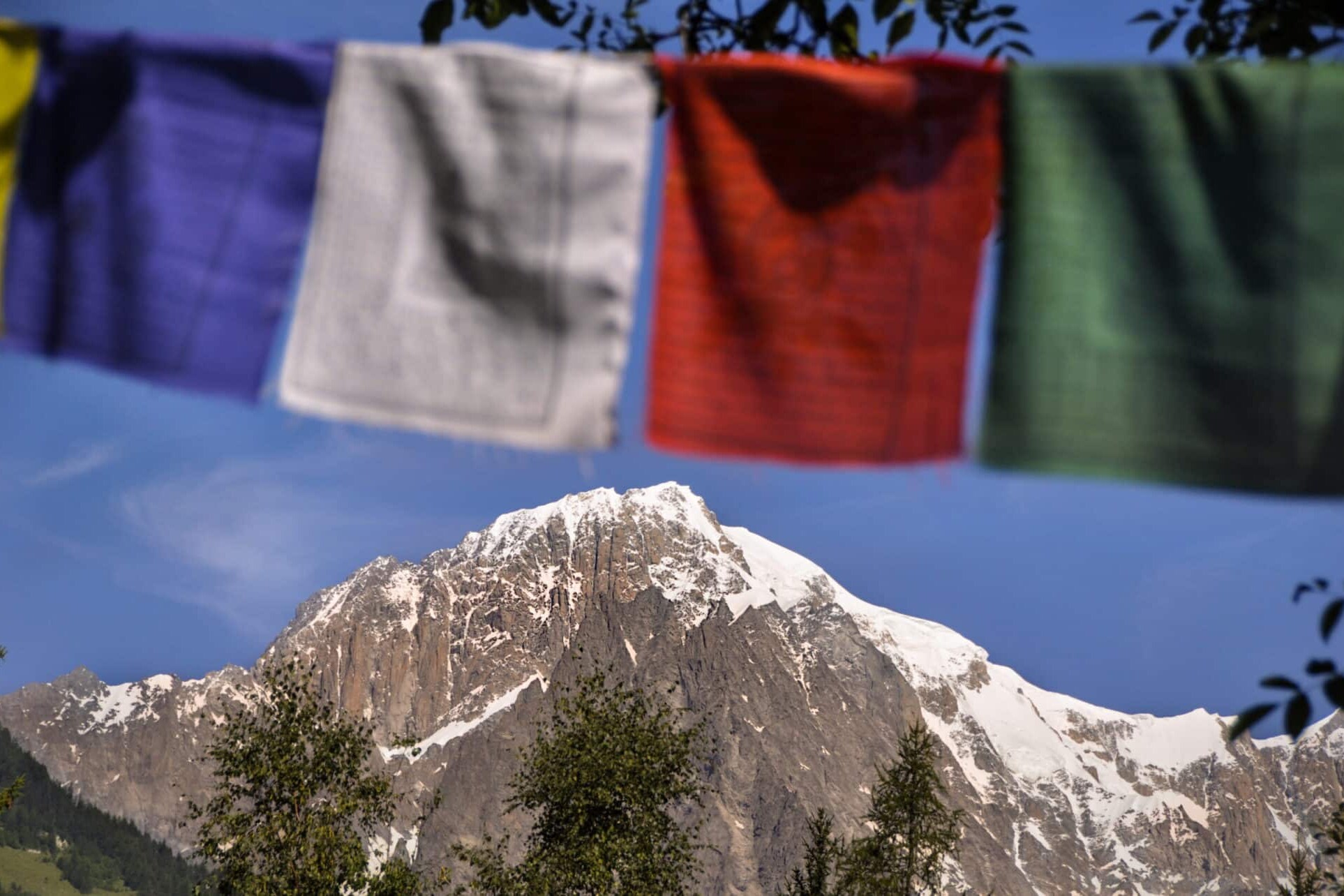 Totem Advenuture Bandiere di preghiera colorate sullo sfondo di montagne innevate sotto un cielo azzurro e limpido invitano all'avventura in Valle d'Aosta, dove vi attendono esperienze all'aria aperta come il kayak. Rafting Kayaking Parapendio Canyoning Valle d’Aosta