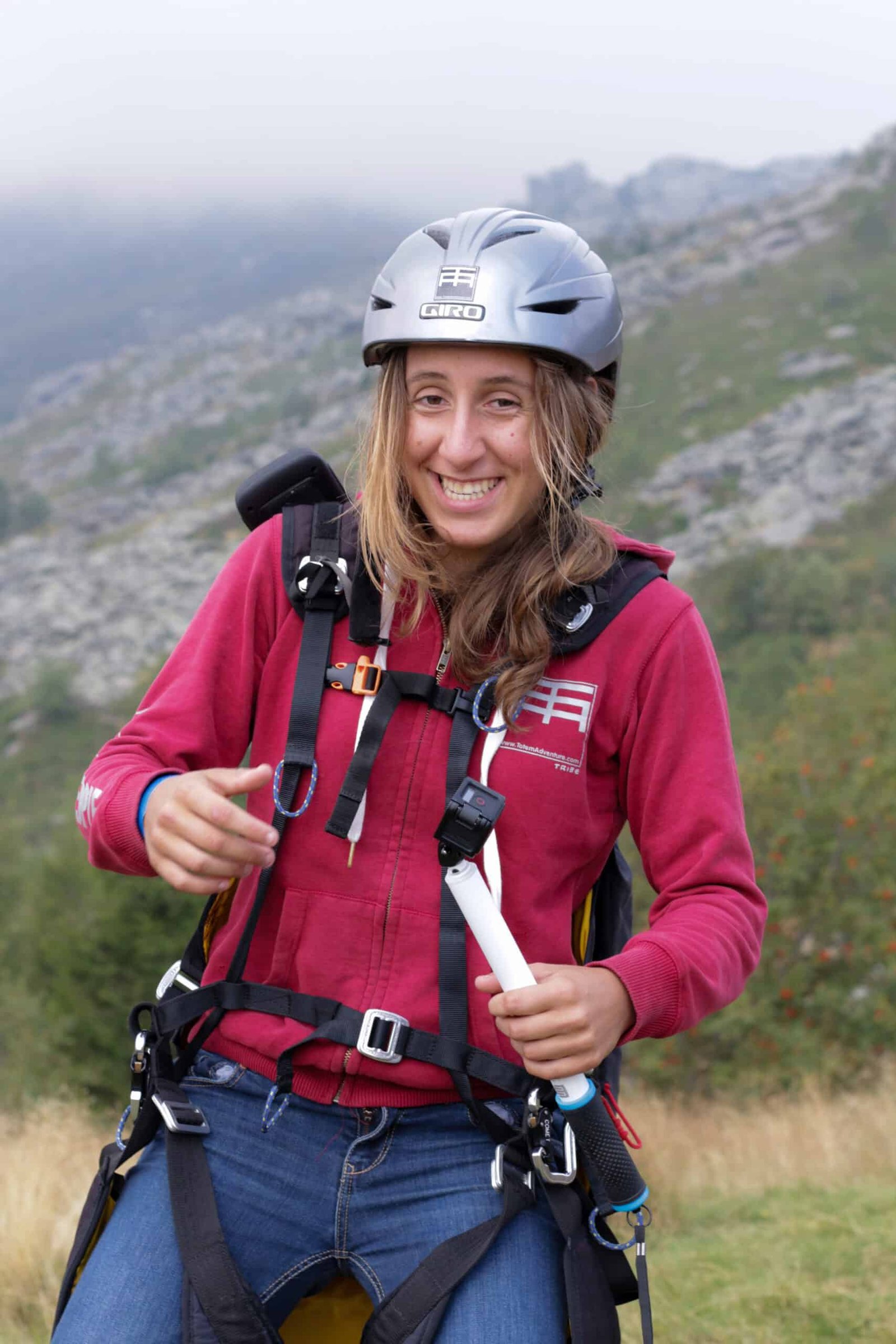 Totem Advenuture With a bright smile in his red hoodie and helmet, the adventurer clutches his paraglider harness against the backdrop of the misty hills of Pre Saint Didier, ready for exciting outdoor experiences in the Aosta Valley. Rafting Kayaking Paragliding Canyoning Aosta Valley