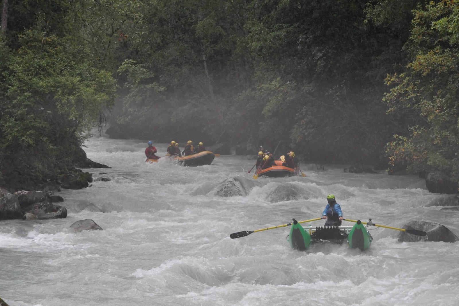 Totem Advenuture Tre zattere con persone che navigano su un fiume veloce e roccioso, circondato da fitti alberi verdi. Rafting Kayaking Parapendio Canyoning Valle d’Aosta