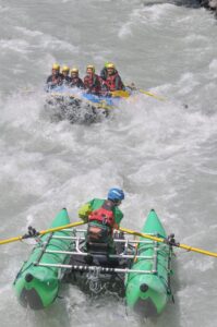 Totem Advenuture Due zattere con persone munite di caschi e giubbotti di salvataggio remano tra le rapide di un fiume. Rafting Kayaking Parapendio Canyoning Valle d’Aosta
