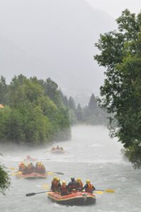 Totem Advenuture Gruppi con caschi gialli che praticano rafting su un fiume avvolto dalla nebbia, circondato da alberi verdi e montagne. Rafting Kayaking Parapendio Canyoning Valle d’Aosta