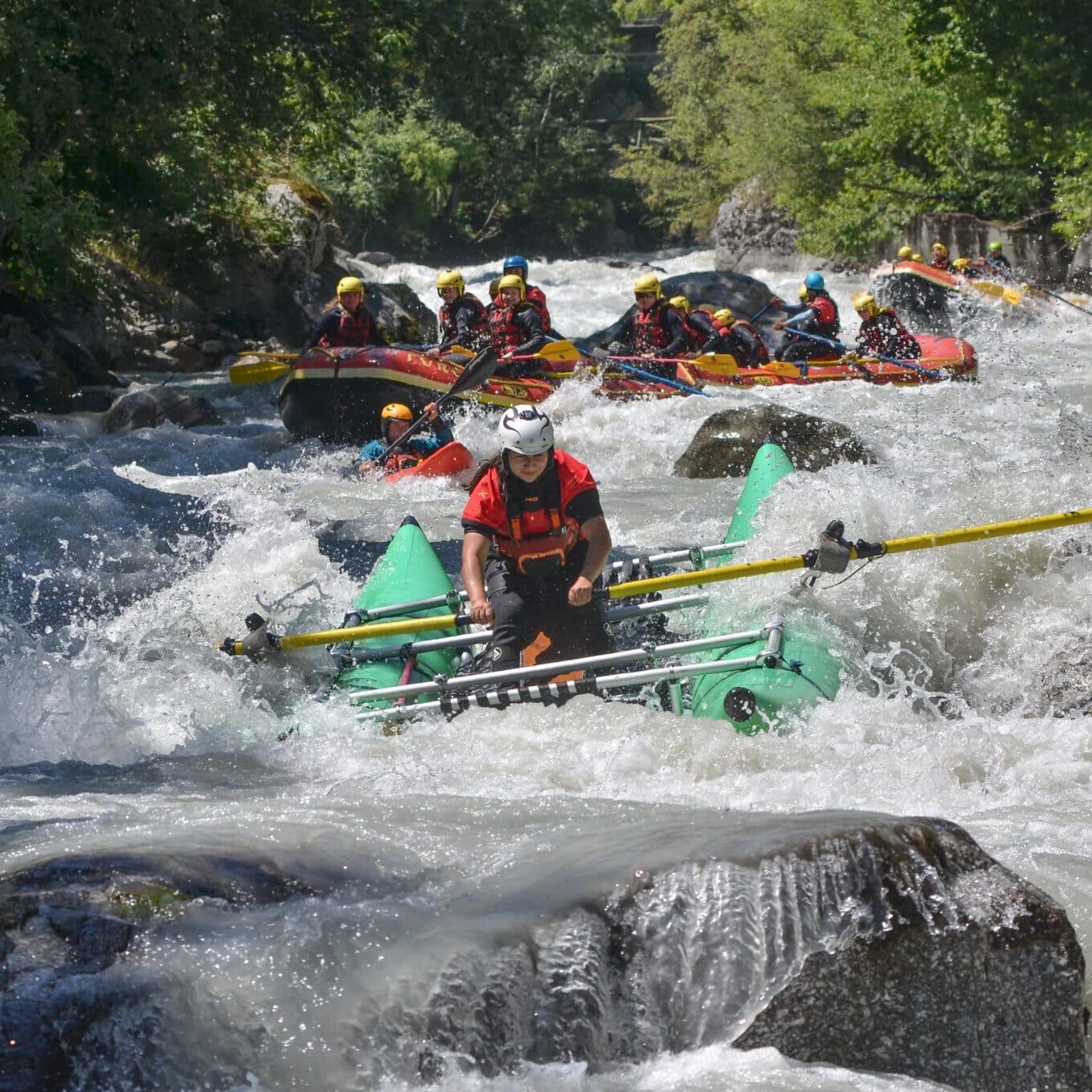Totem Advenuture Persone con caschi e giubbotti di salvataggio affrontano le rapide su gommoni gonfiabili, circondati da rocce. Rafting Kayaking Parapendio Canyoning Valle d’Aosta